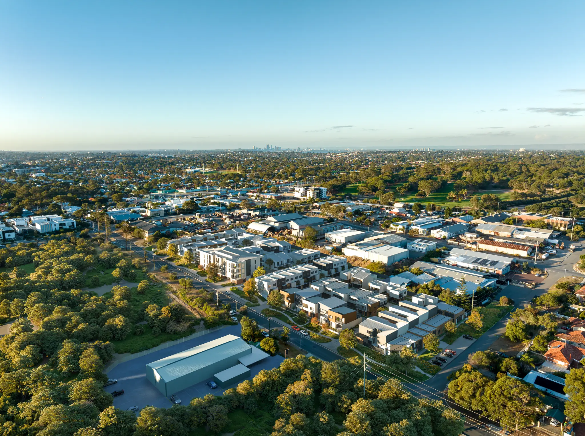 Large-scale aerial photomontage communicating the layout, building forms, streets, landscaping and broader urban context of a contemporary multi-residential precinct. High-resolution aerial architectural photomontage of a contemporary residential precinct integrated into an established urban and parkland setting